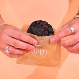 Hands holding a Double Choc Chip New York Cookie in a Crumbs & Doilies branded paper bag.